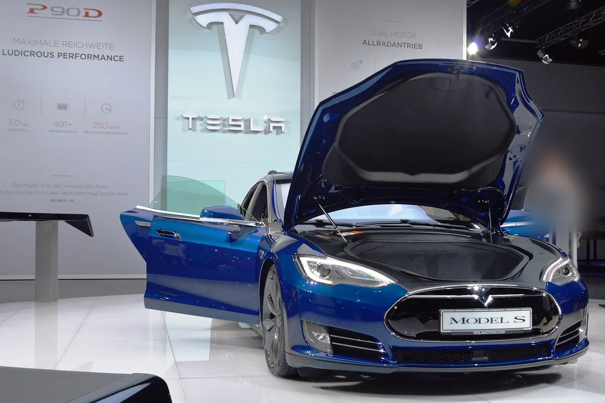 A blue Tesla Model S with its front trunk and doors open at a motor show